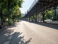 an empty street next to a bridge in a city with some people walking on the road