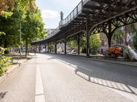 an empty street next to a bridge in a city with some people walking on the road