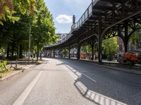 an empty street next to a bridge in a city with some people walking on the road