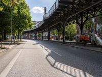 an empty street next to a bridge in a city with some people walking on the road