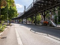 an empty street next to a bridge in a city with some people walking on the road