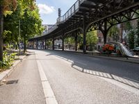 an empty street next to a bridge in a city with some people walking on the road