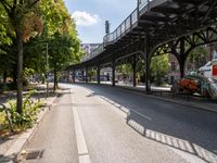 an empty street next to a bridge in a city with some people walking on the road