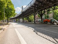 an empty street next to a bridge in a city with some people walking on the road