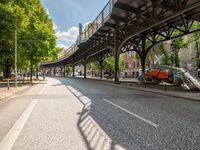 an empty street next to a bridge in a city with some people walking on the road