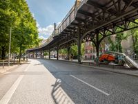 an empty street next to a bridge in a city with some people walking on the road