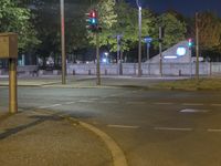 a traffic light on an empty street at night with green lights, trees and benches