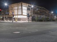 an empty street is lit up at night, including traffic light, sidewalk and building