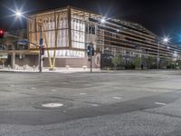 an empty street is lit up at night, including traffic light, sidewalk and building