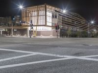 an empty street is lit up at night, including traffic light, sidewalk and building