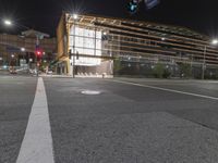 an empty street is lit up at night, including traffic light, sidewalk and building