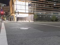 an empty street is lit up at night, including traffic light, sidewalk and building