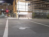an empty street is lit up at night, including traffic light, sidewalk and building