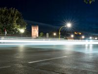 an empty street at night, with an urban clock tower in the background behind it