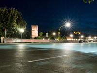 an empty street at night, with an urban clock tower in the background behind it