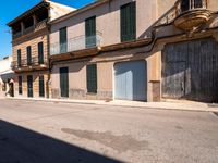 an empty street has old, boarded buildings and doors on each side of it and another large building with balconies