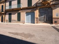 an empty street has old, boarded buildings and doors on each side of it and another large building with balconies