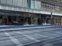 a street is empty, with cars parked in the sun on both sides of the road