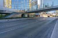 a view of an empty street with a pedestrian bridge over it in the background and skyscrapers