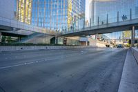 a view of an empty street with a pedestrian bridge over it in the background and skyscrapers