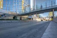 a view of an empty street with a pedestrian bridge over it in the background and skyscrapers