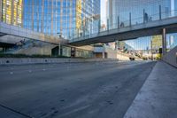 a view of an empty street with a pedestrian bridge over it in the background and skyscrapers