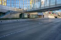 a view of an empty street with a pedestrian bridge over it in the background and skyscrapers