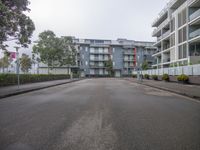 empty street with no traffic in front of tall building on either side of road and fence with bushes outside