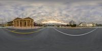 the intersection of an empty street with clouds and buildings in the background is empty and cloudy