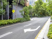 an empty street with a yellow arrow sign near tall buildings and lush green trees lining the street