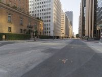 an empty city street with tall buildings and cars parked in the middle of the road