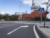 a street sign near an empty street with a ship in the background by some trees