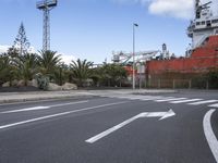 a street sign near an empty street with a ship in the background by some trees