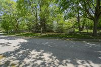 an empty street is empty in the shade of trees and grass surrounding it, surrounded by an open gate and fence