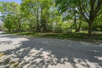 an empty street is empty in the shade of trees and grass surrounding it, surrounded by an open gate and fence