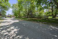 an empty street is empty in the shade of trees and grass surrounding it, surrounded by an open gate and fence