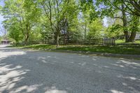 an empty street is empty in the shade of trees and grass surrounding it, surrounded by an open gate and fence