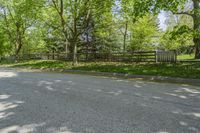 an empty street is empty in the shade of trees and grass surrounding it, surrounded by an open gate and fence