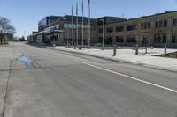 an empty street in front of a commercial building with flags flying from the ground and two trees at the corner