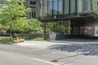 an empty street next to tall glass buildings and trees in front of a city building