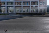 an empty street near a building with some cars parked on the sidewalk in front of it