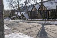 the street is empty with snow on the ground and houses next to it the tree branch casts a shadow