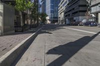 an empty street in an urban area with buildings, bushes and a bench to sit in