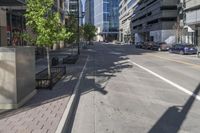 an empty street in an urban area with buildings, bushes and a bench to sit in