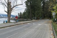 an empty street next to a body of water near some trees and a sidewalk with people walking