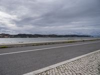 an empty street next to some water on the side of the road with cloudy skies