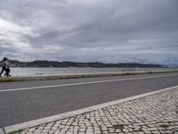 an empty street next to some water on the side of the road with cloudy skies