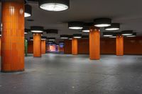 an empty underground train station with several lamps above it and orange tiled floors below each of them