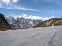 an empty tarmac on the top of a mountain road with snow capped mountains in the background