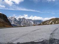 an empty tarmac on the top of a mountain road with snow capped mountains in the background